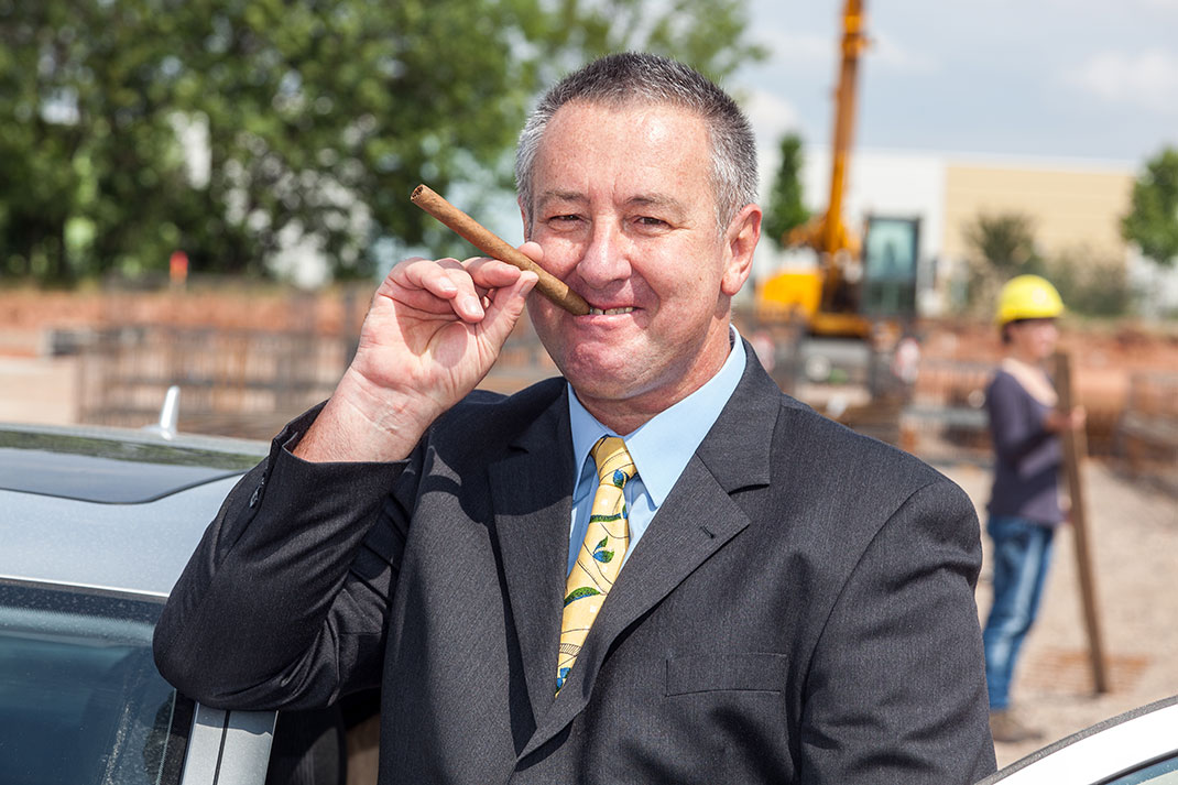 Un patron fumant un cigare devant un ouvrier via Shutterstock