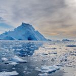 Iceberg monumental et fragments de glace flottant sur une mer partiellement dégelée en Antarctique sous un ciel voilé