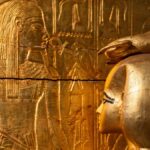 Statue dorée égyptienne avec vautour sacré devant une fresque gravée