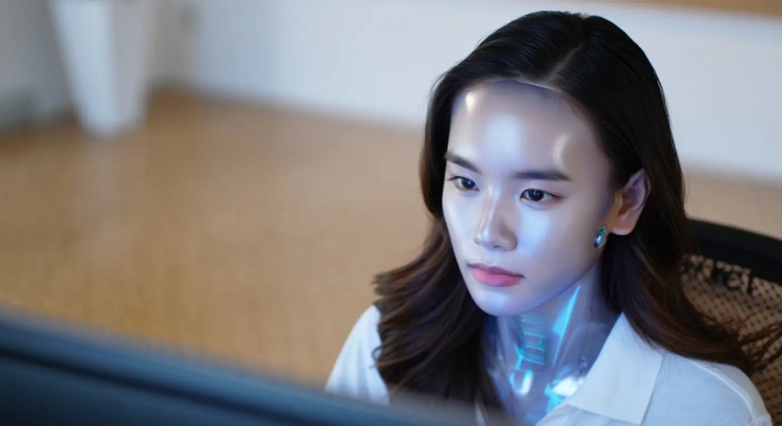 Femme robot humanoïde au visage métallique travaillant devant un écran d’ordinateur.