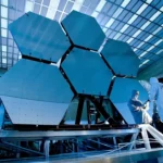 Des ingénieurs en combinaison stérile ajustent les miroirs hexagonaux du télescope James Webb dans un laboratoire de la NASA