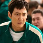 Homme inquiet en combinaison verte dans une scène de Squid Game entouré d'autres participants