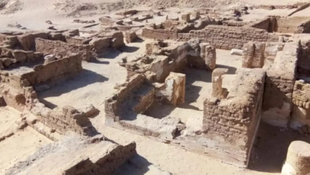 Vestiges d’une cité antique découverts dans le désert égyptien, montrant des murs en briques et ruines d’habitations révélées par les fouilles archéologiques.