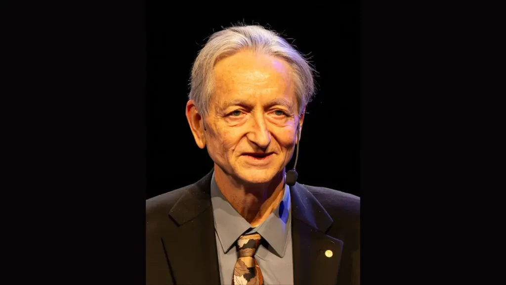 Portrait de Geoffrey Hinton, scientifique reconnu et lauréat du prix Turing, lors d’une conférence, portant un micro-casque et un costume sombre.