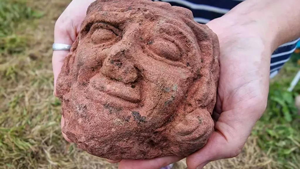 Gros plan sur une tête sculptée ancienne en pierre tenue dans des mains.