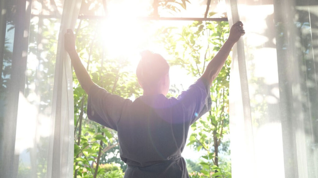 Une femme qui tire les rideaux le matin