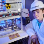 Jackson Oswalt, adolescent en blouse de laboratoire, pose à côté de son réacteur de fusion nucléaire artisanal.