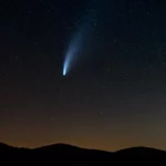 Comète lumineuse avec une longue traînée observée dans le ciel nocturne au-dessus des montagnes.