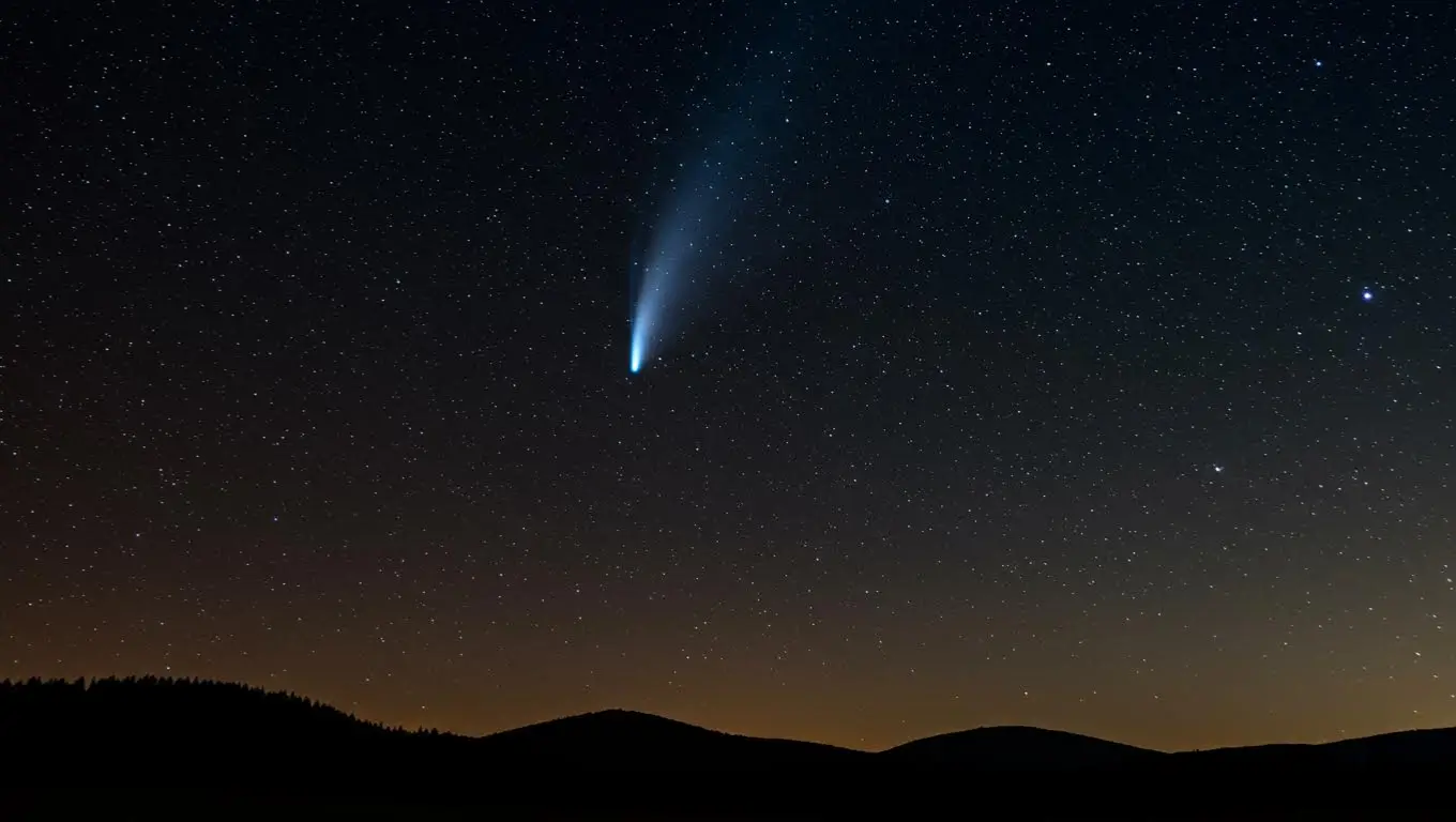 Comète lumineuse avec une longue traînée observée dans le ciel nocturne au-dessus des montagnes.