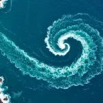 Vue aérienne d’un tourbillon géant dans l’océan, formant une spirale parfaite d’écume blanche.