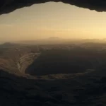 Vue depuis une grotte ou un tunnel volcanique sur Vénus, montrant un paysage rocheux et un cratère géant sous une lumière orangée rappelant l’atmosphère de la planète.