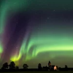 Aurores boréales vertes et violettes illuminant un ciel étoilé au-dessus d’une église et d’une forêt, lors d’un rare phénomène visible en France.