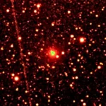 Image astronomique de la comète interstellaire 3I/ATLAS au centre d’un champ étoilé, photographiée en lumière infrarouge avec une croix verte indiquant sa position.