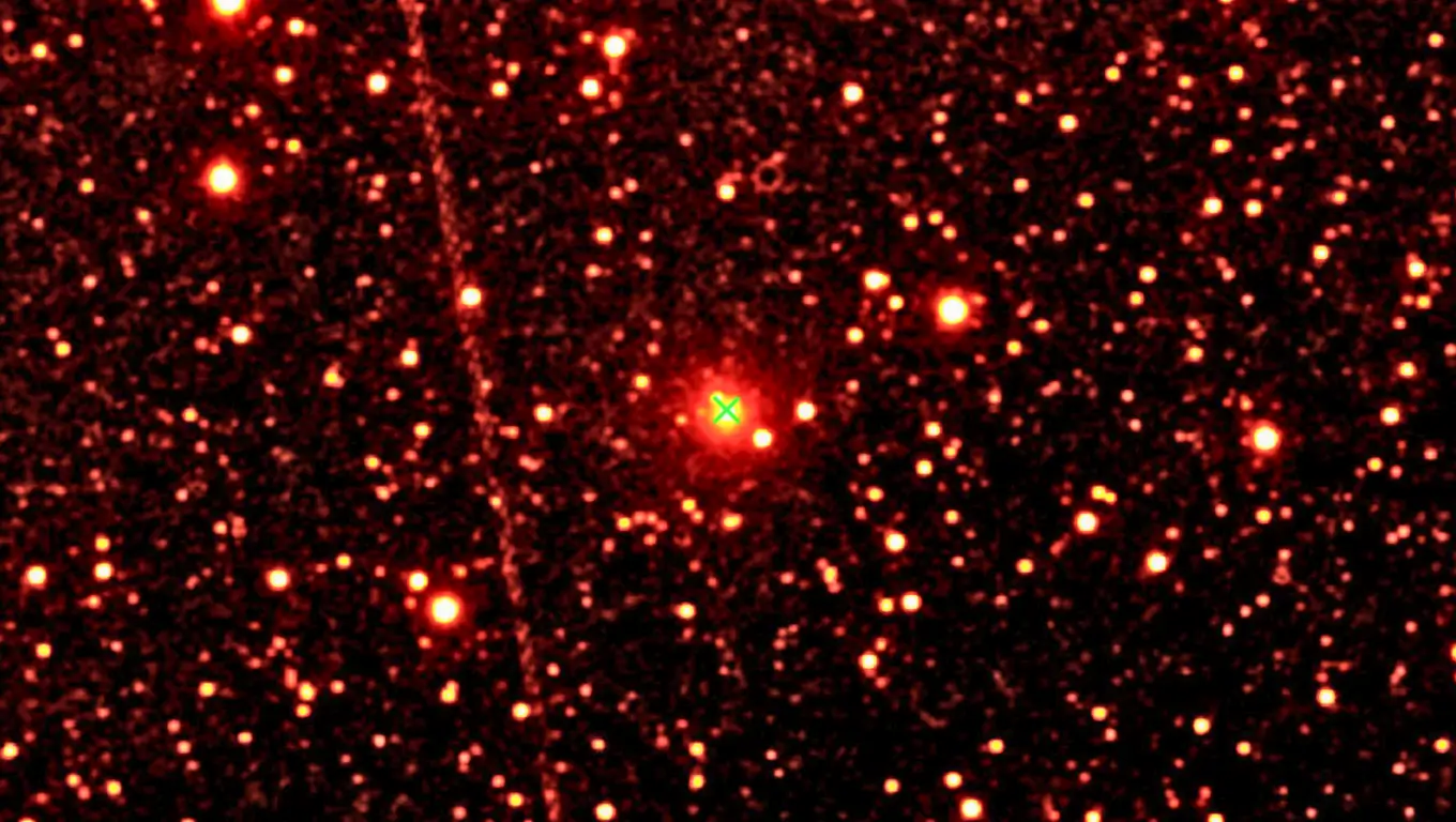 Image astronomique de la comète interstellaire 3I/ATLAS au centre d’un champ étoilé, photographiée en lumière infrarouge avec une croix verte indiquant sa position.