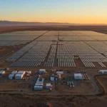 Vue aérienne d’une immense centrale solaire dans le désert, avec d’innombrables panneaux photovoltaïques alignés en rangées régulières.