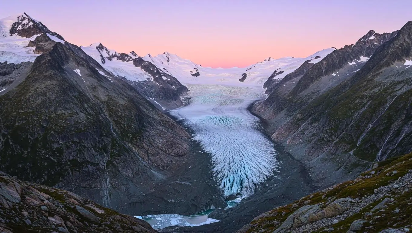 Vue d’un glacier alpin descendant entre deux chaînes de montagnes, éclairé par une lumière rosée au lever du soleil.