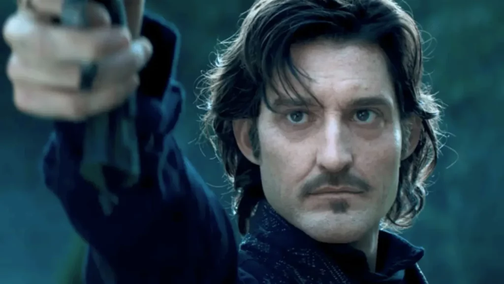 Homme au regard sérieux pointant une arme vers l’avant, dans un décor sombre.