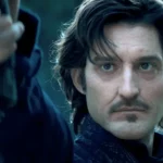 Homme au regard sérieux pointant une arme vers l’avant, dans un décor sombre.