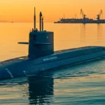 Sous-marin naviguant en surface au coucher du soleil, avec un port industriel et des grues en arrière-plan.