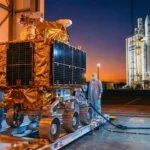 Rover de l’ESA en préparation dans un hangar avec des ingénieurs, et fusée Ariane prête au lancement au coucher du soleil