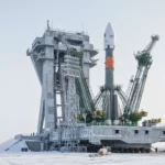 Fusée dressée sur un pas de tir à Baïkonour, entourée de structures métalliques et grues, dans un paysage enneigé sous un ciel clair.