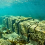 Alignement de blocs de pierre immergés formant un mur sous-marin ancien, recouvert d’algues et de faune marine