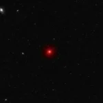 Champ profond de l’Univers montrant un point lumineux rouge isolé au milieu de galaxies lointaines et d’un fond étoilé sombre