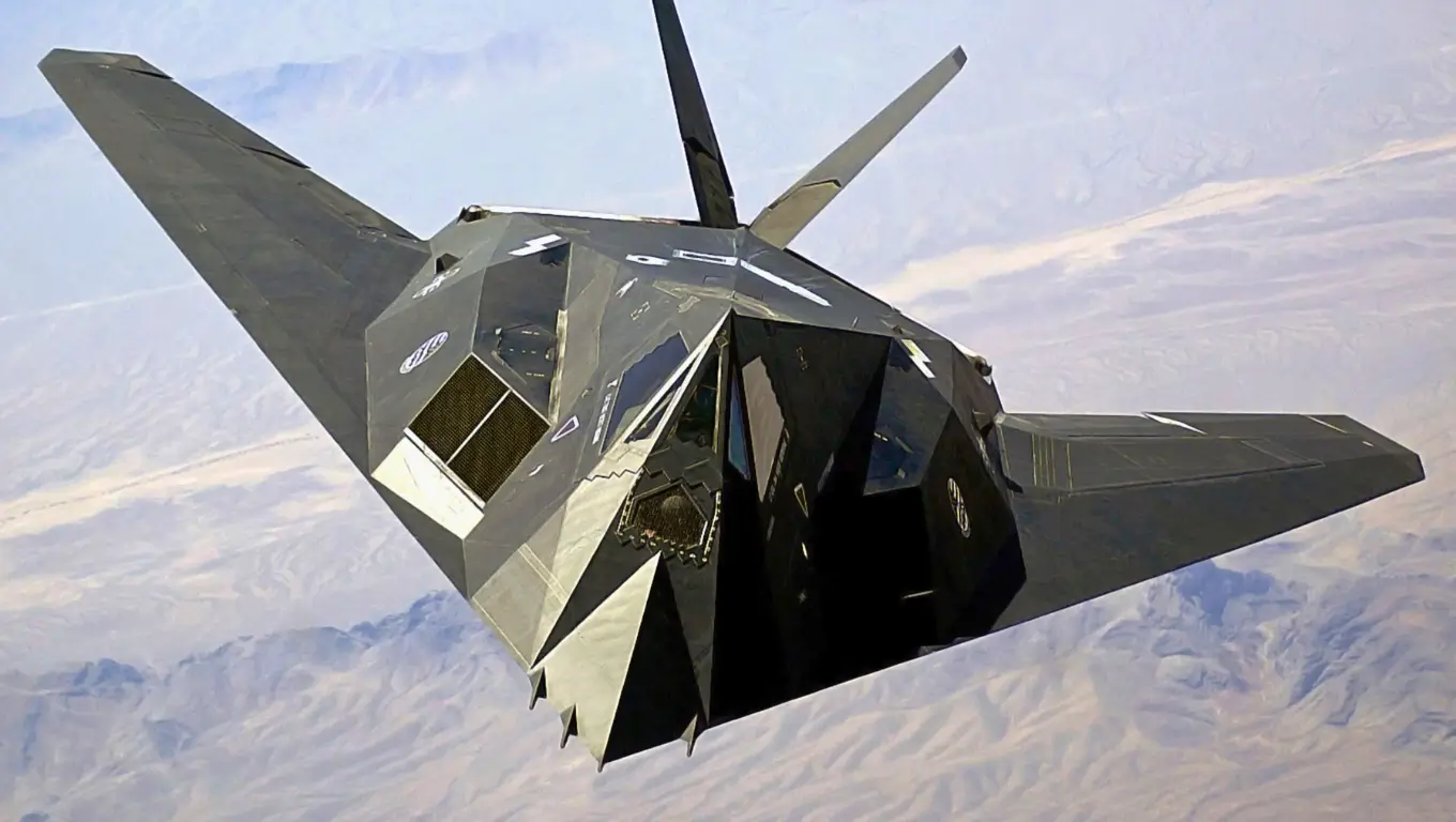 Avion furtif F-117 Nighthawk en vol au-dessus d’un paysage désertique, illustrant la technologie de furtivité radar.