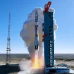 Fusée chinoise en plein décollage depuis une base désertique, avec une forte fumée blanche et des flammes visibles sous le lanceur.