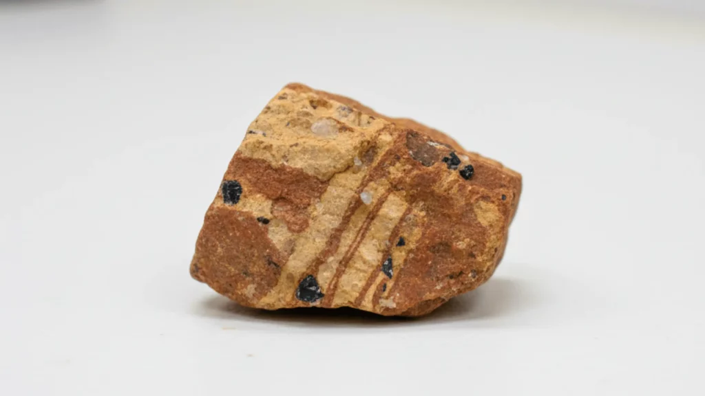 Roche naturelle striée de beige et marron rougeâtre, avec inclusions de minéraux noirs et cristal de quartz. Spécimen géologique.