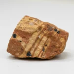 Roche naturelle striée de beige et marron rougeâtre, avec inclusions de minéraux noirs et cristal de quartz. Spécimen géologique.