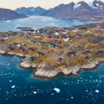 Village côtier du Groenland entouré de glace flottante, illustrant l’impact du réchauffement climatique et de la fonte de la calotte glaciaire.