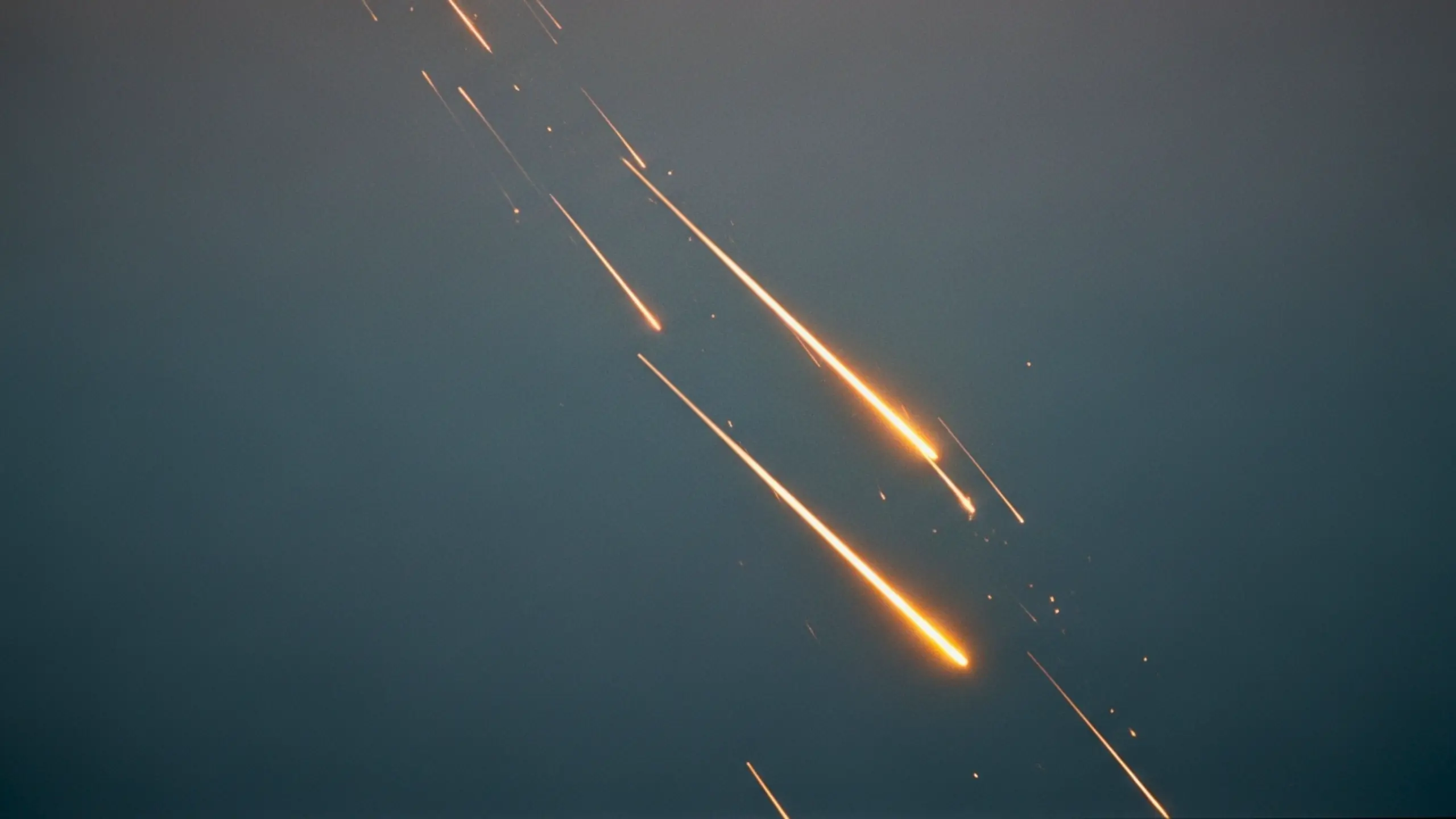 Plusieurs traînées lumineuses de débris incandescents traversant un ciel sombre, évoquant une rentrée atmosphérique après une explosion.