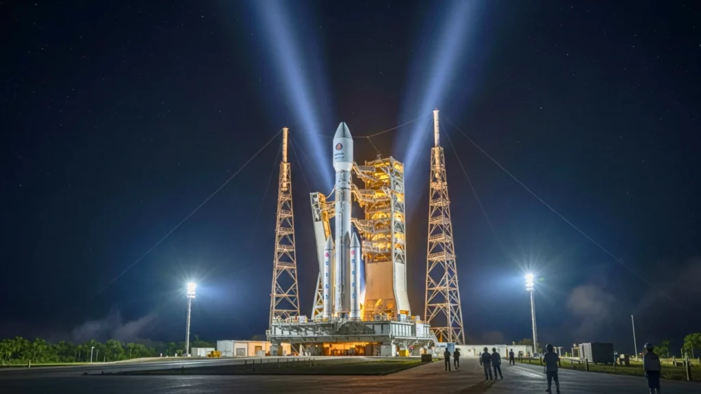 Fusée Ariane éclairée par des projecteurs sur son pas de tir de nuit, entourée de structures métalliques et de personnel au sol.