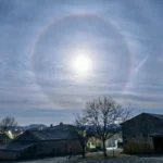 Halo circulaire autour de la Lune dans un ciel voilé, au-dessus de maisons et d’arbres d’un village rural en Charente.