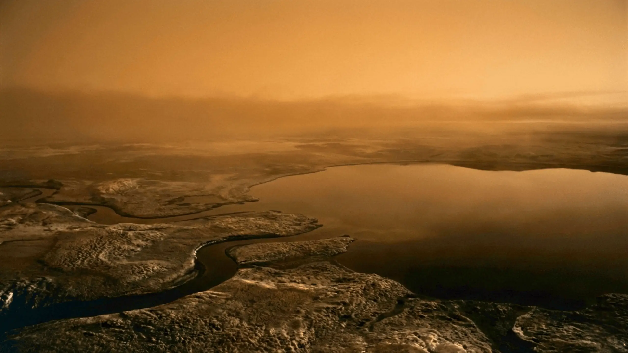 Paysage de Titan avec des étendues de liquides et des formations géologiques sous une atmosphère orangée et brumeuse.