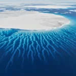 Vue aérienne d’une plateforme de glace en Antarctique montrant des canyons sous-marins visibles par les reliefs de l’eau en bordure de la calotte