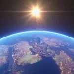 Vue de la Terre depuis l’espace avec le Soleil brillant à l’horizon et les continents éclairés.