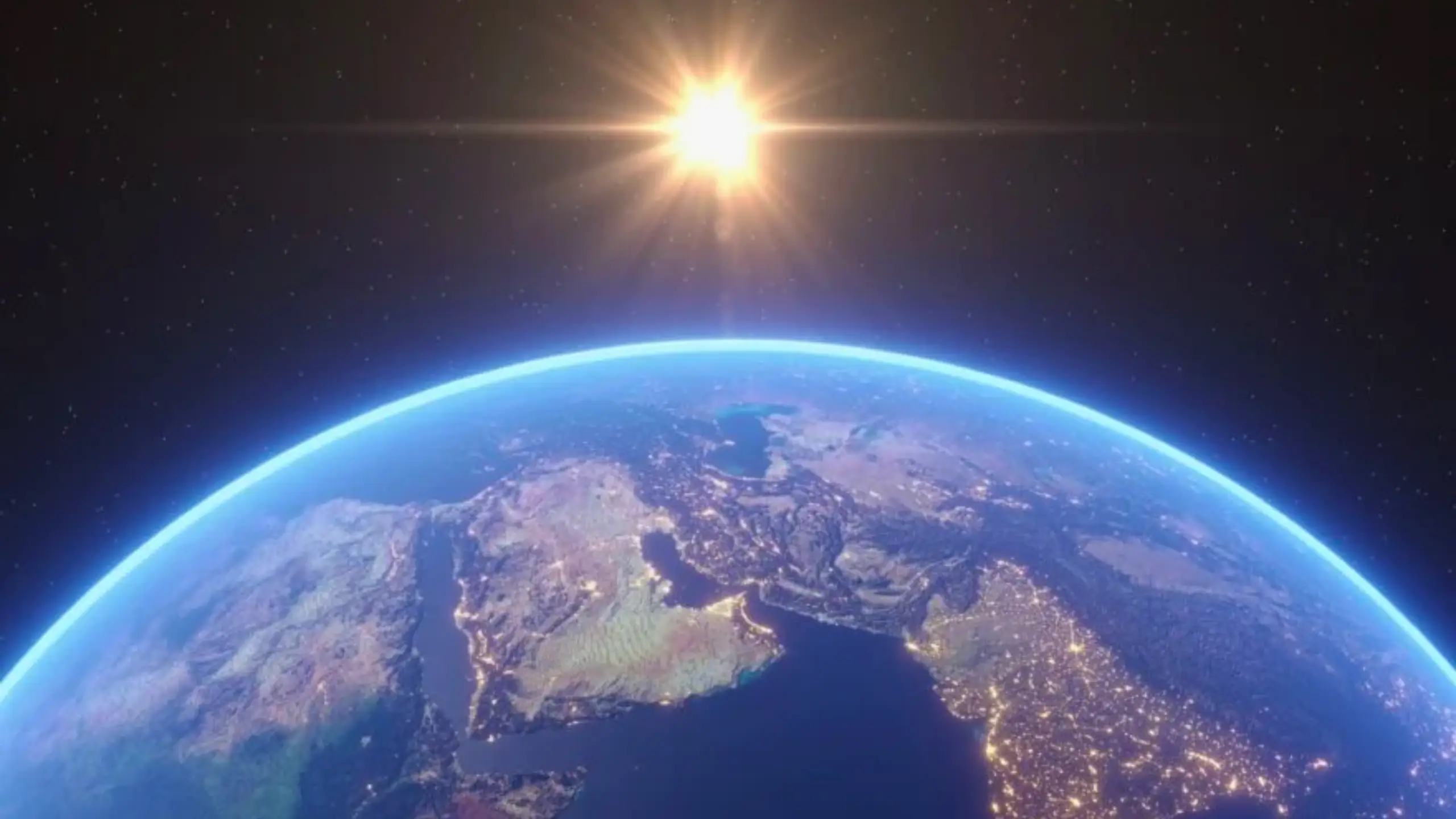 Vue de la Terre depuis l’espace avec le Soleil brillant à l’horizon et les continents éclairés.