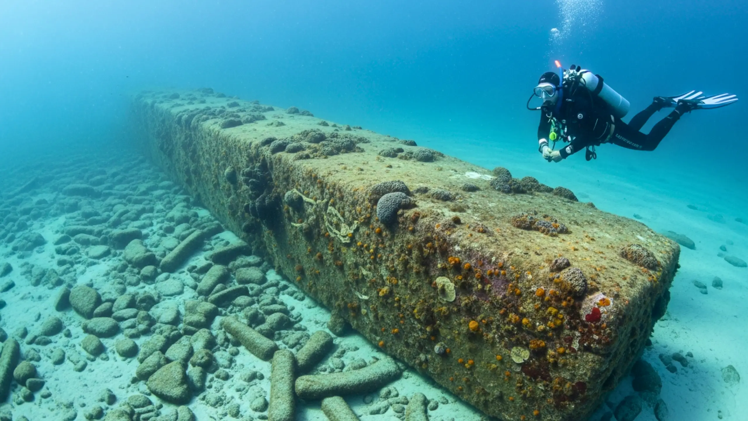 Plongeur explorant un long mur de pierre immergé recouvert de coraux, découvert à faible profondeur au fond de l’océan