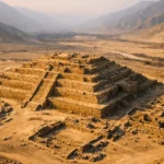 Vue aérienne de la cité antique de Caral au Pérou, avec une grande pyramide en gradins au cœur d’une vallée désertique.