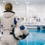 Astronaute européenne en combinaison spatiale, vue de dos, s’entraînant dans un bassin de simulation en centre spatial avant une mission orbitale