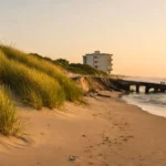 Plage sableuse en recul avec dune érodée, ouvrage côtier et immeuble en arrière-plan face à la mer