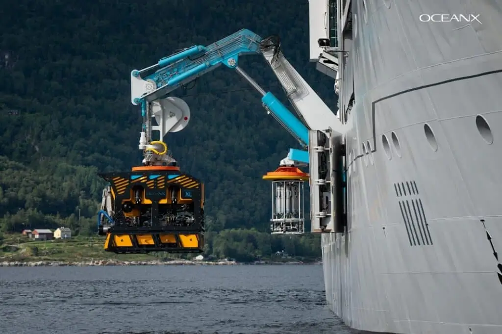 Un bras robotisé du navire OceanX déploie un robot sous-marin scientifique au-dessus de la mer pour une mission d’exploration océanique.