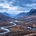 Vue panoramique des Highlands écossais avec une vallée sauvage et une rivière sinueuse sous un ciel nuageux dramatique.