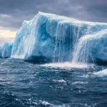 Un iceberg massif flotte dans l’océan Austral, sa surface glacée se fissurant tandis que l’eau sombre l’entoure.