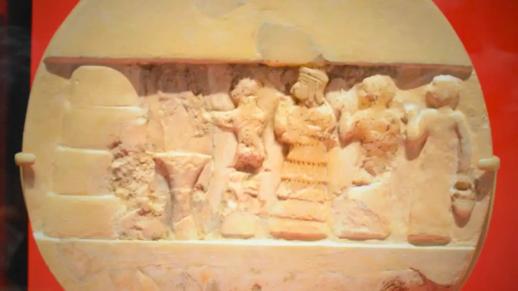 Bas-relief en albâtre montrant Enheduanna, grande prêtresse d’Ur, participant à un rituel religieux en Mésopotamie antique.