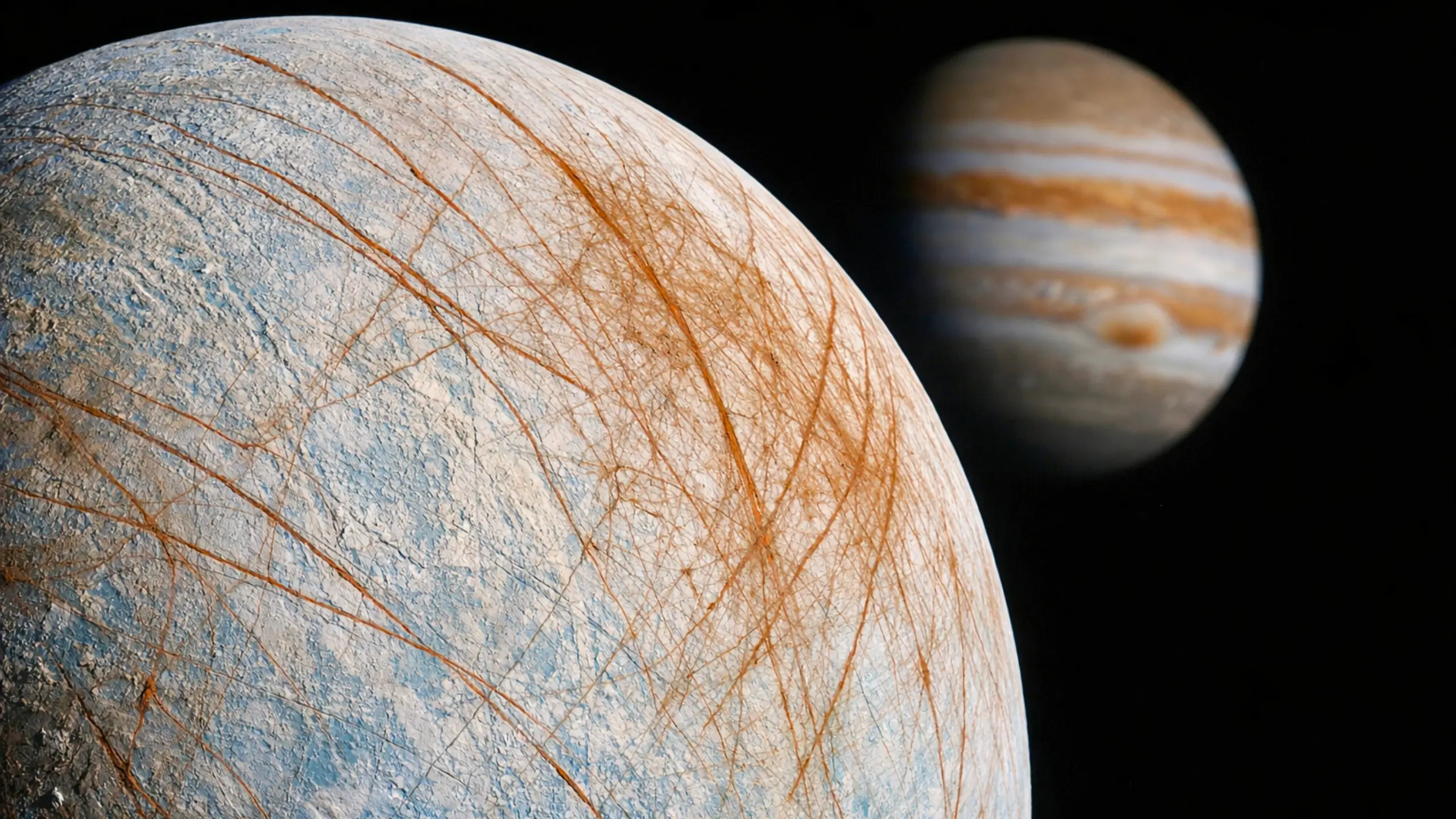 Vue réaliste de la lune Europe montrant sa surface glacée striée de fractures, avec Jupiter en arrière-plan dans l’espace.