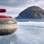 Pierre de curling en granite sur la glace avec l’île volcanique d’Ailsa Craig en arrière-plan sous un ciel écossais nuageux.