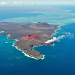 Vue aérienne d’une île volcanique active entourée d’océan turquoise, avec coulées de lave et cratères, illustrant la tectonique des plaques et ses effets sur la vie marine.